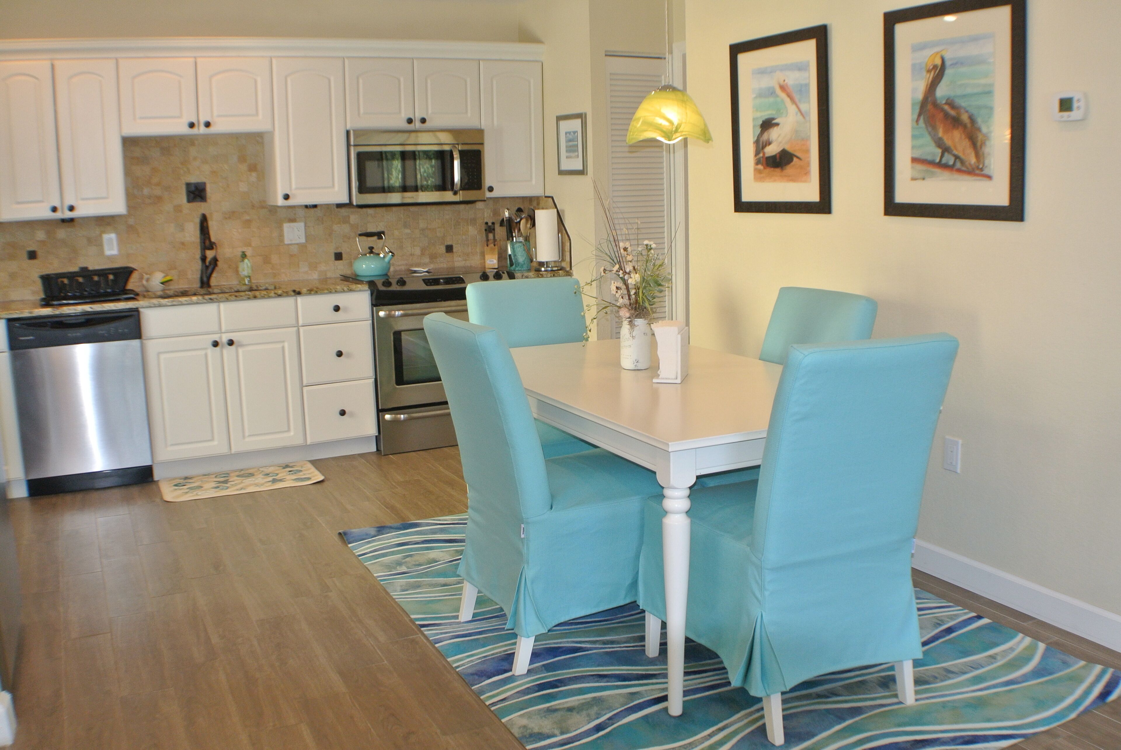 Una cocina moderna con armarios blancos, electrodomésticos de acero inoxidable y una zona de comedor con mesa y sillas.