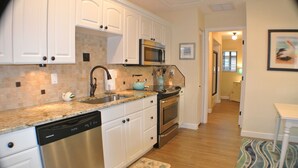 Una cocina con gabinetes blancos, electrodomésticos de acero inoxidable, encimera de granito y suelo de madera.