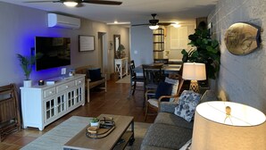 A modern living room with a TV, sofa, coffee table, and ceiling fans. -  Crew Rest Maui - 2BR/2BA, Oceanfront, Superior Views, A/C, sleeps 6 (Wailuku)