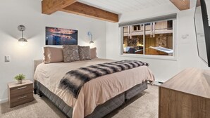 Un dormitorio con cama, lámparas de noche, una ventana con vistas y techo con vigas a la vista.