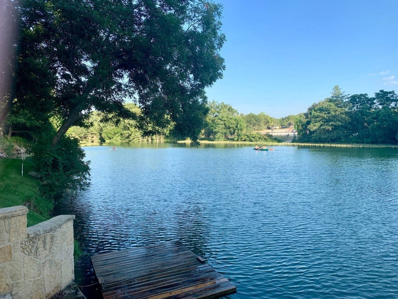 Un lago tranquillo con un molo di legno che si protende nell'acqua, circondato da una vegetazione lussureggiante e alberi.