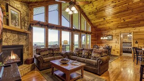 A cozy log cabin interior with a stone fireplace, leather sofas, and a dining area. - 4 bedroom 4 bathroom sleeps 14 outdoor pool access great mountain views and free internet access (Sevierville)