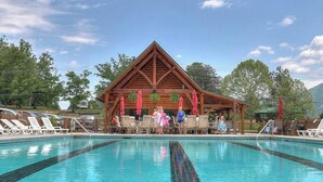 A pool area with lounge chairs and a wooden building with a triangular roof. - 4 bedroom 4 bathroom sleeps 14 outdoor pool access great mountain views and free internet access (Sevierville)