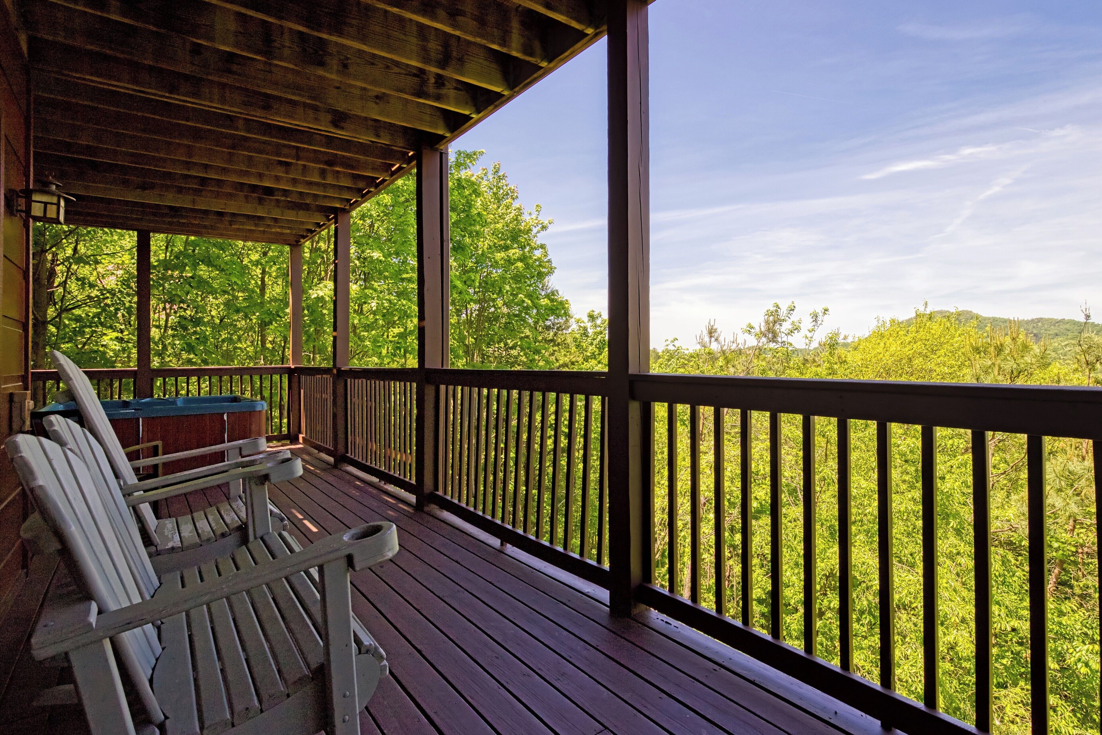 A wooden deck with two Adirondack chairs and a table, overlooking a forested area.