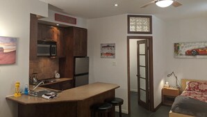 A compact kitchen with a central island, a dining area, and a bedroom with a bed and nightstand. - Cute and  Cozy basement unit in Tremblant (Mont-Tremblant)