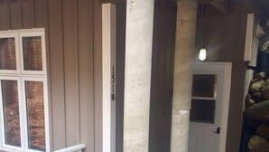 A covered patio area with a wooden deck, a white railing, and a stone pillar. - Cute and  Cozy basement unit in Tremblant (Mont-Tremblant)