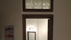 A bathroom with a dark tiled floor, a white sink with a mirror above it, and a small cabinet below. There is a framed artwork on the wall to the left. - Cute and  Cozy basement unit in Tremblant (Mont-Tremblant)