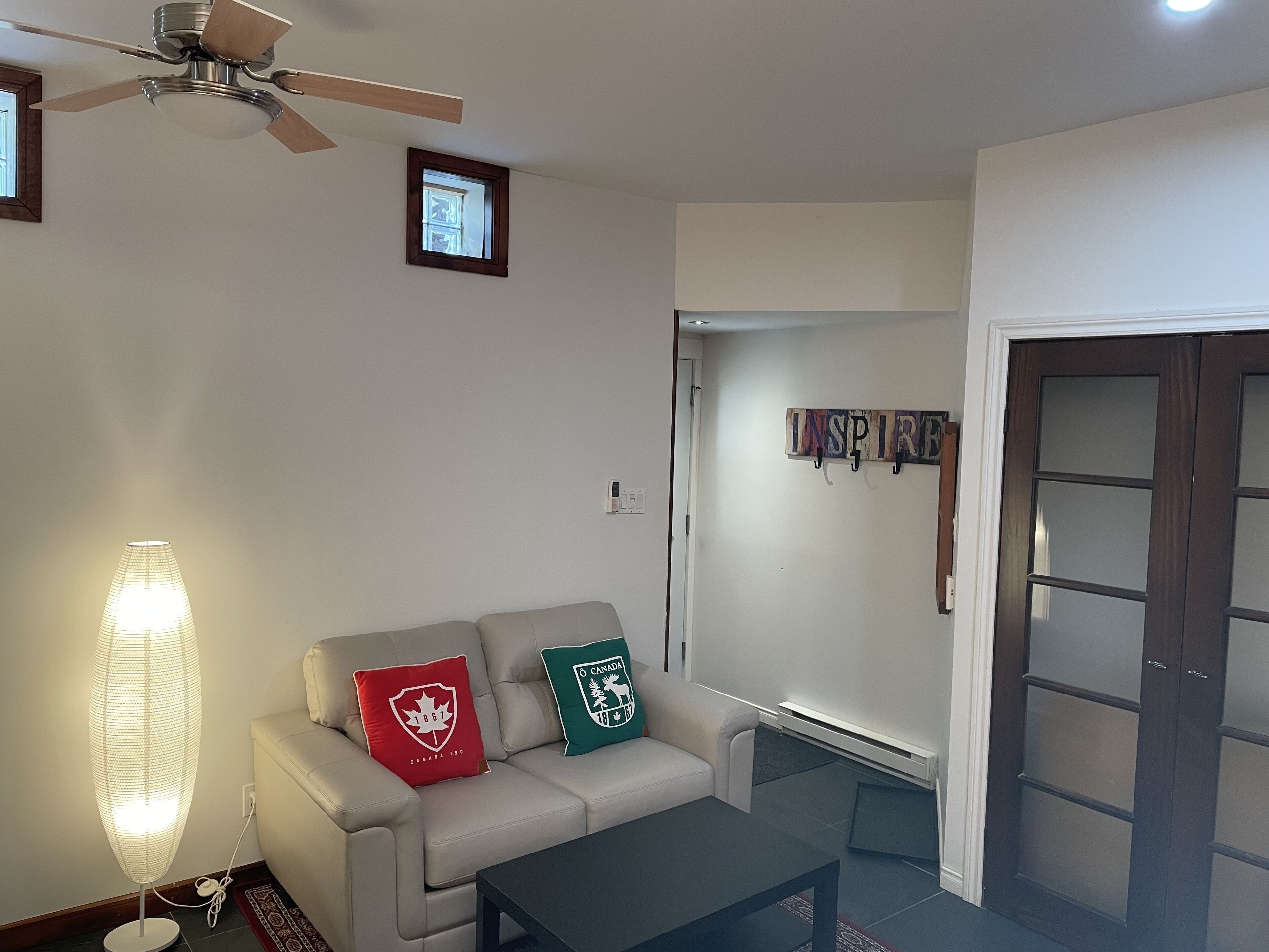 Un soggiorno con ventilatore a soffitto, un divano con due cuscini, una lampada da terra e una porta con finestra.