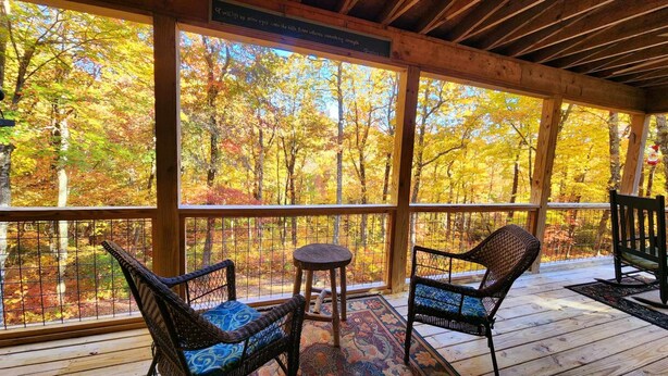 A wooden deck with wicker chairs and a small table, overlooking a forest with autumn foliage. - The Mountains are calling for You and Yours!
      (Cleveland)