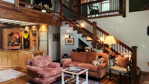 A spacious living area with a wooden floor, a staircase, and a kitchen area. - The Mountains are calling for You and Yours!
      (Cleveland)