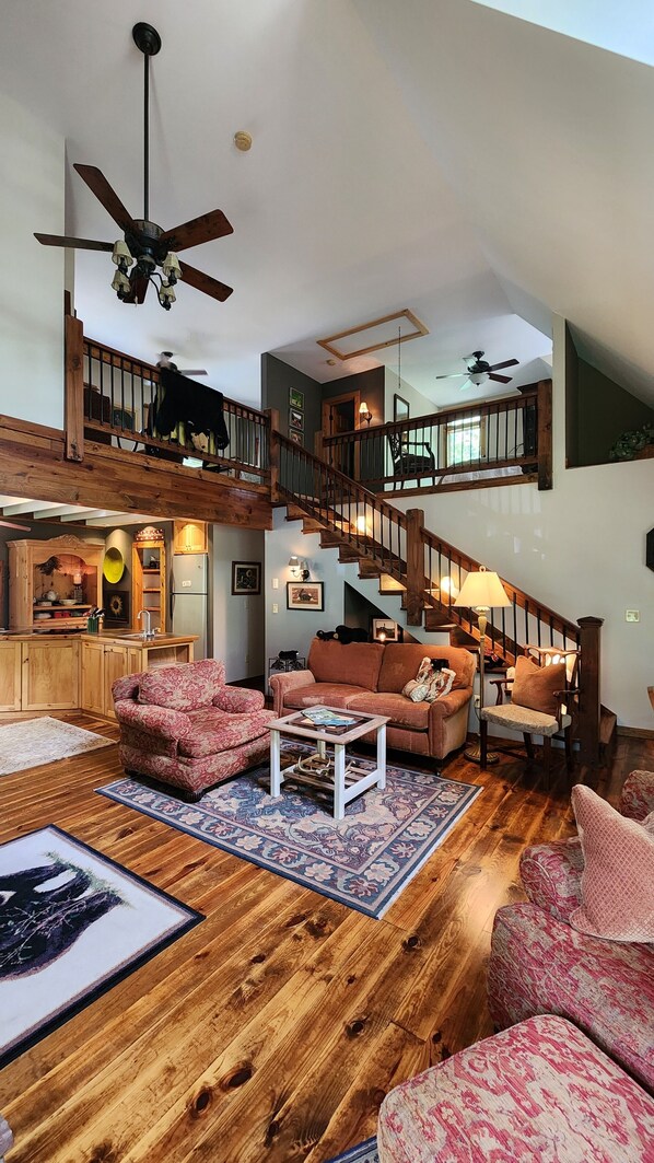 A spacious living area with a wooden floor, a staircase, and a kitchen area.