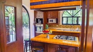 A kitchen with wooden cabinets, a microwave, a gas stove, and a fruit bowl on the island. - French-Colonial Villa,Close to Paseo Montejo, Hotels and Restaurants! (Mérida)