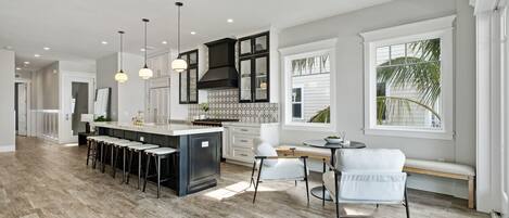 A modern kitchen with a central island, bar stools, pendant lighting, and a view of the outdoors.