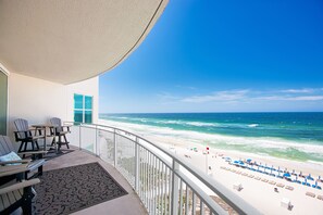 A balcony with a view of the ocean, beach chairs, and a table.