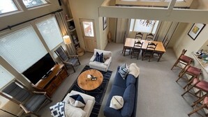 A spacious living area with a large TV, comfortable seating, a dining table, and a high ceiling with skylights.