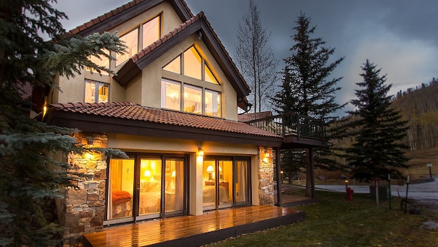 A modern two-story house with large windows, a stone facade, and a wooden deck.