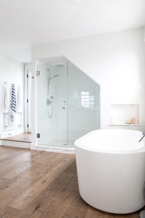 Ein modernes Badezimmer mit einer großen Badewanne, einer gläsernen Dusche, Holzboden und einer weißen Farbgestaltung.