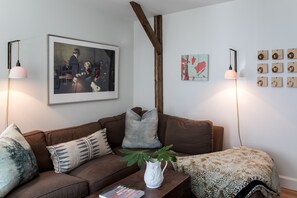 Ein Wohnzimmer mit einem braunen Sofa, einem Couchtisch mit einem Buch, einer weißen Vase mit einer Pflanze und Wandkunst.