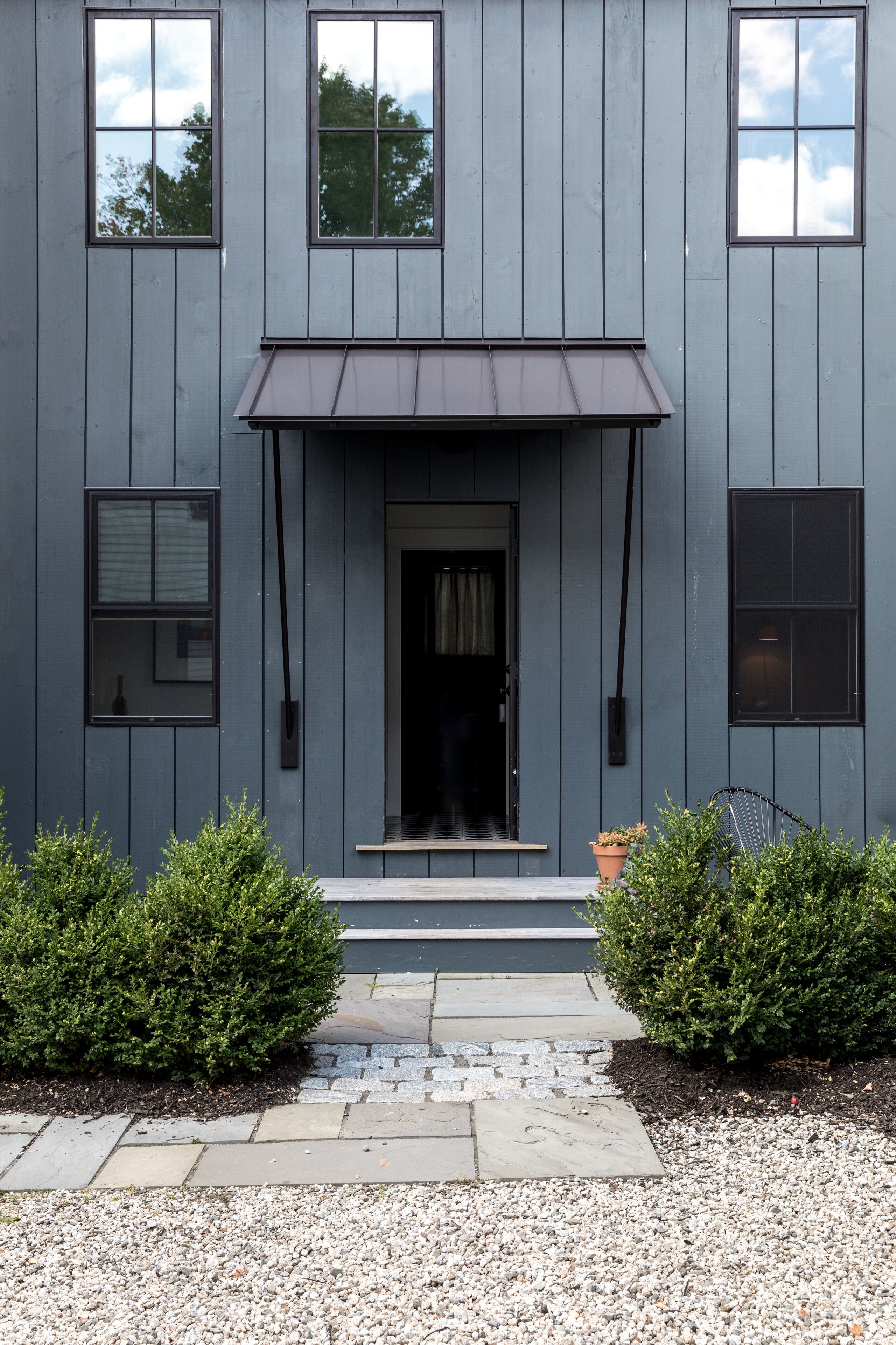 A modern two-story building with a dark gray facade, a central entrance with a small porch, and a gravel driveway.