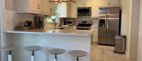 A modern kitchen with white cabinetry, stainless steel appliances, and a central island with stools.
