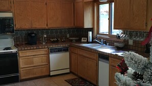 A kitchen with wooden cabinets, a dishwasher, and a sink. There is a Christmas tree with ornaments and a sign that reads "CABIN". - Walk To Slopes & Restaurants! (Angel Fire)