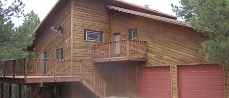 A two-story wooden house with a balcony, a garage, and a staircase leading to the main entrance.