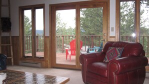 A living room with a red leather chair, a wooden coffee table, and a sliding glass door leading to an outdoor deck. - Walk To Slopes & Restaurants! (Angel Fire)