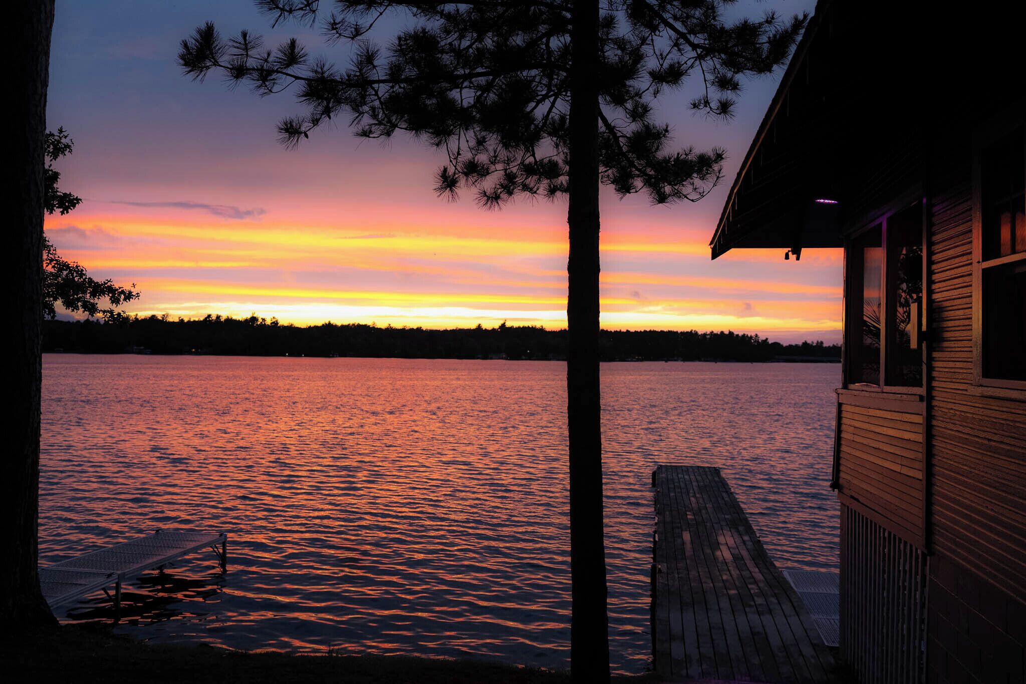 A wooden dock extending into a body of water with a sunset in the background.
