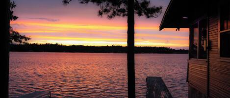 A wooden dock extending into a body of water with a sunset in the background.