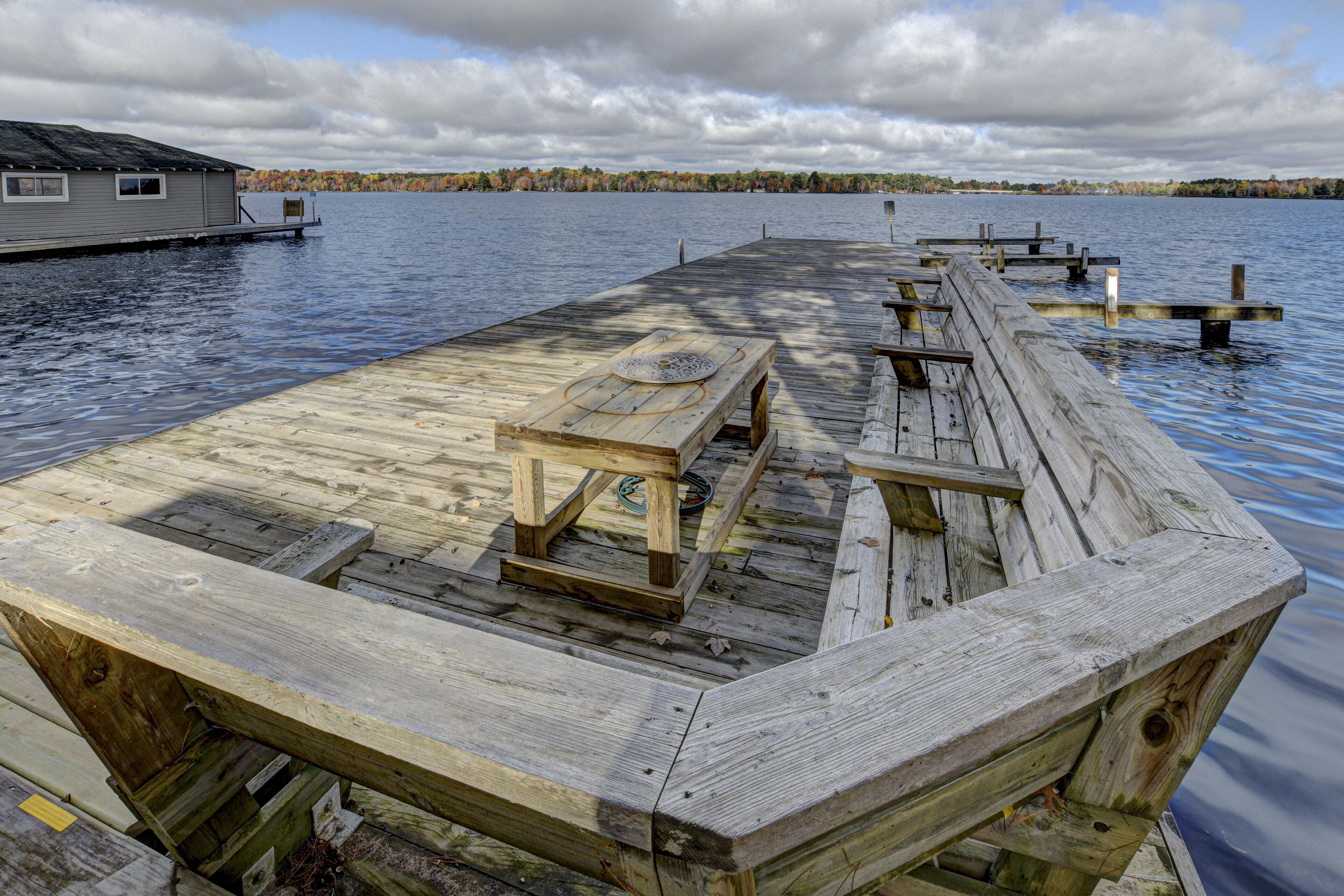A wooden dock with a picnic table and benches, extending over calm water.