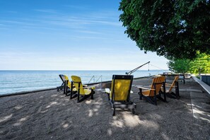 A row of Adirondack chairs facing a body of water, with a picnic table and a fishing rod visible. - Sunsets by the Bay - Your Waterfront Oasis (Leamington)