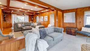 L’intérieur chaleureux d’un chalet avec des murs en bois, un canapé gris, un banc en bois et une table à manger.