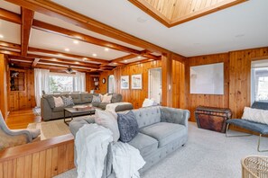 A cozy cabin interior with wooden walls, a grey sofa, a wooden bench, and a dining table.