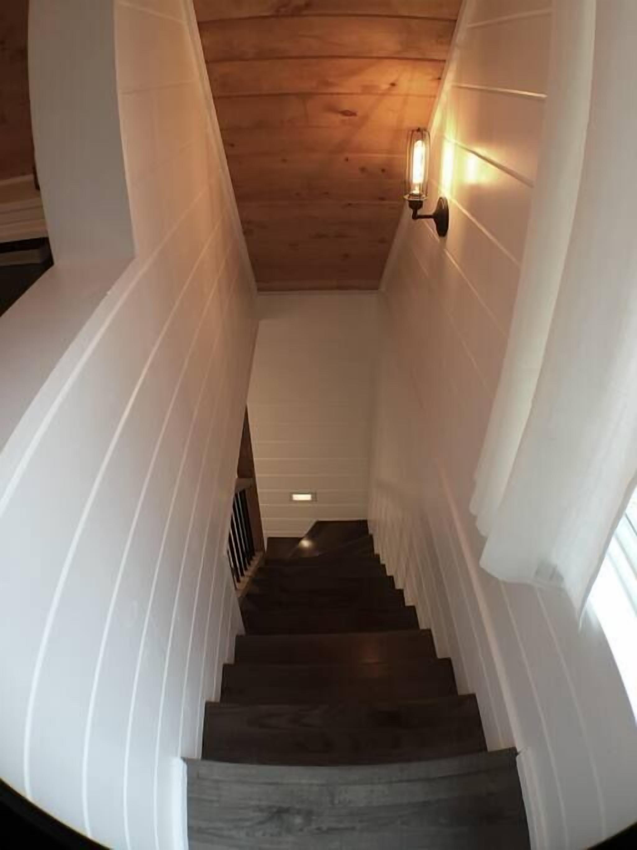 Una escalera de madera con paredes blancas que conduce a una plataforma con una lámpara.