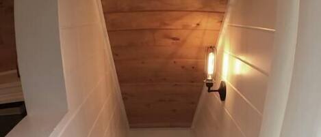 Una escalera de madera con paredes blancas que conduce a una plataforma con una lámpara.