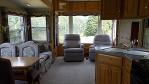 A compact RV interior with a dining area, two sofas, a kitchen with wooden cabinets, and a ceiling fan. - Private RV Camping on the Connecticut River with local mountain views!! (Monroe)