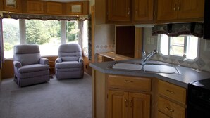 A compact kitchen with wooden cabinets, a sink, and two armchairs. - Private RV Camping on the Connecticut River with local mountain views!! (Monroe)