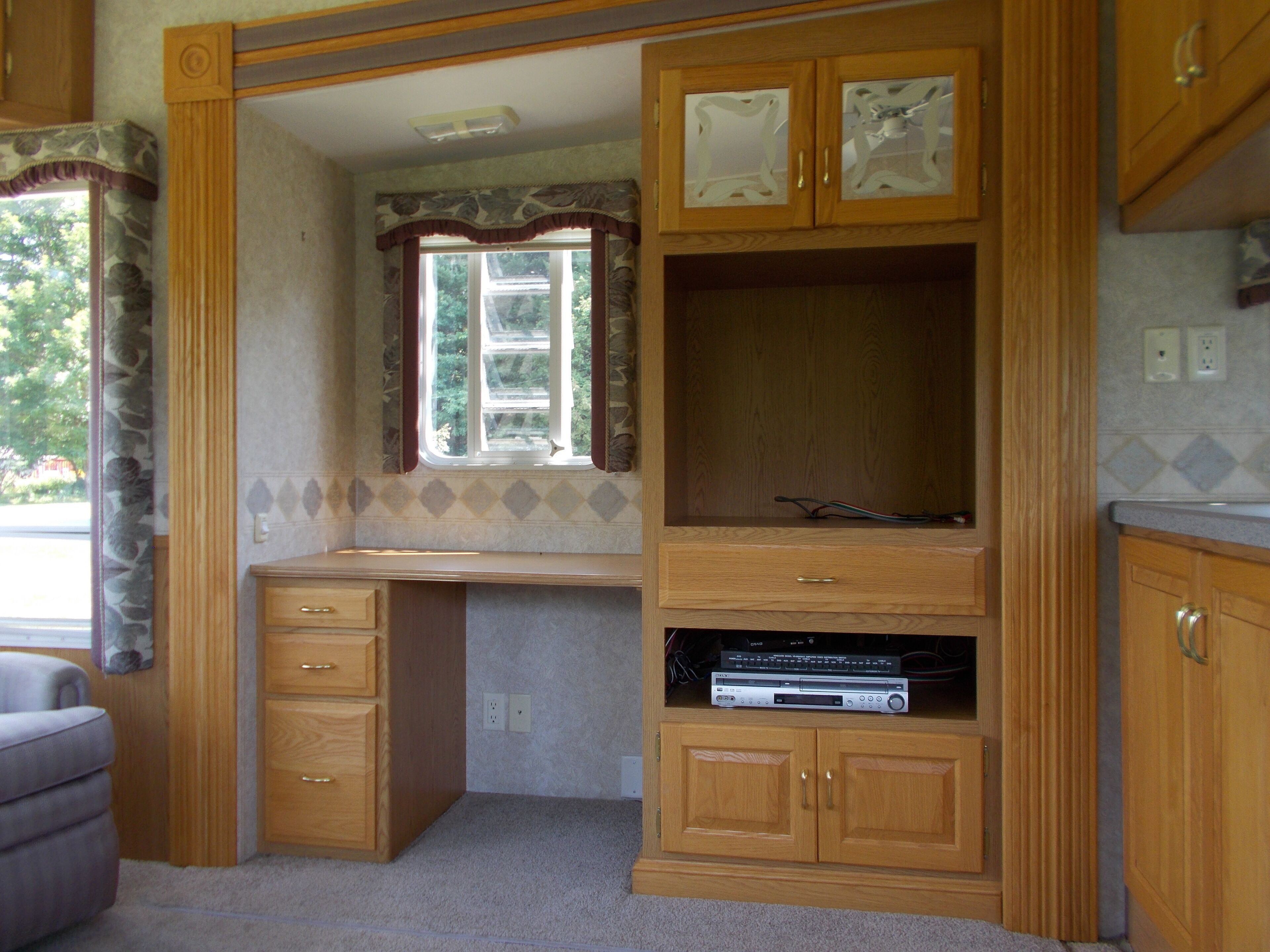 A compact kitchen with wooden cabinets, a built-in countertop, and a window with a view of greenery.