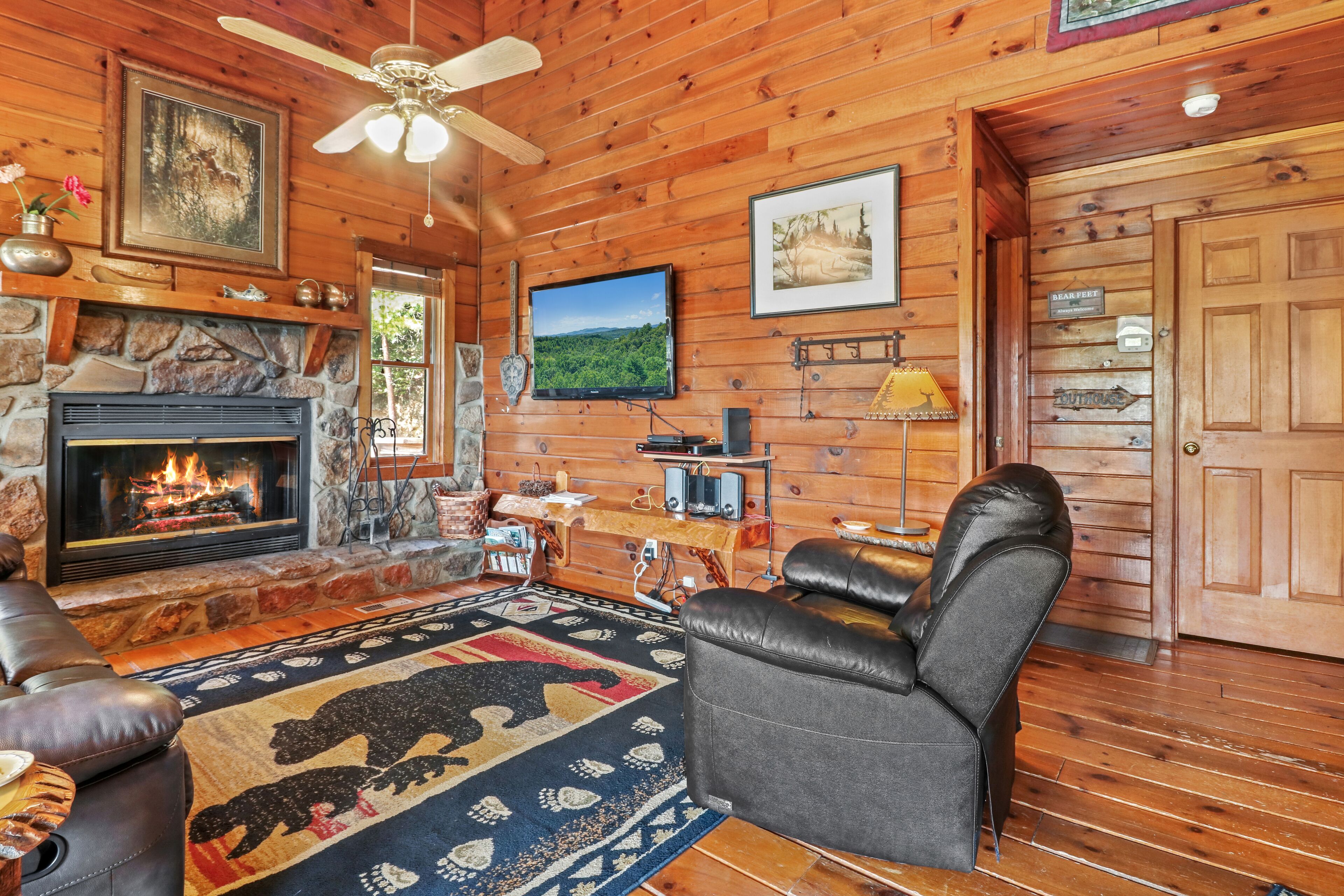 A cozy cabin interior with a fireplace, leather seating, a mounted television, and wooden walls.