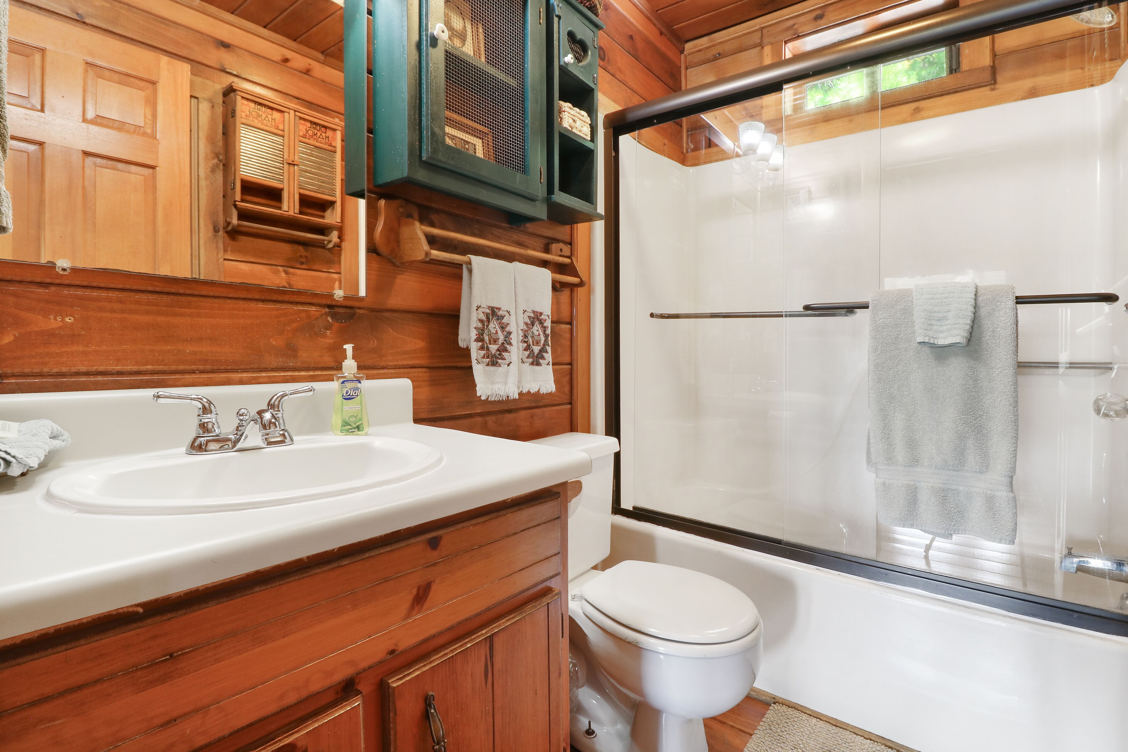 Une salle de bain rustique, aménagée dans une cabane en bois, avec un lavabo, des toilettes et une douche à parois de verre.