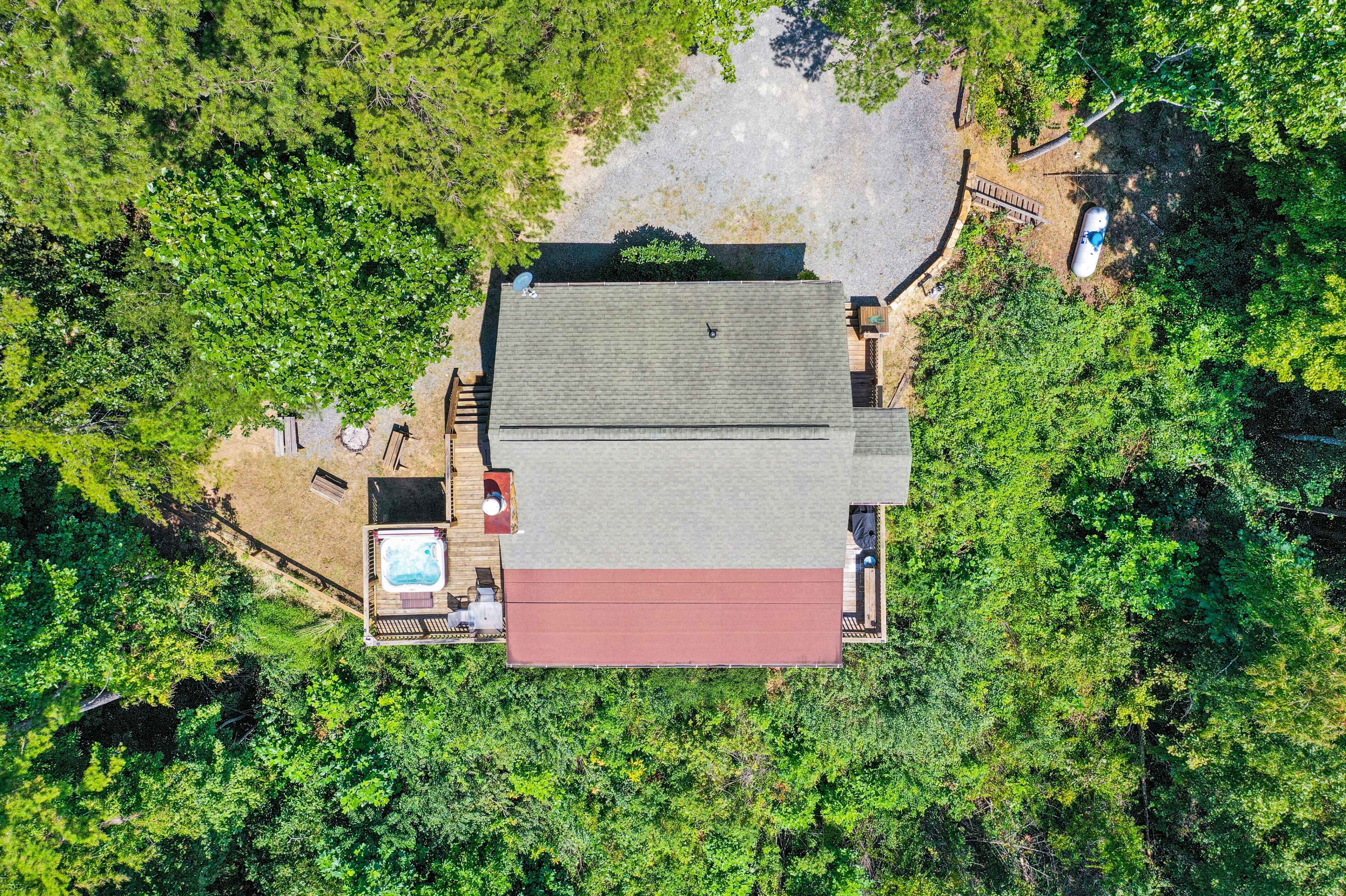 An aerial view of a house with a swimming pool, surrounded by dense greenery.