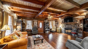A rustic cabin interior with a leather sofa, armchairs, a fireplace, and a stone wall. - AUTHENTIC ANTIQUE LOG CABIN LOCATED IN TIMBERIDGE COMMUNITY (Gatlinburg)