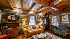 A cozy log cabin interior with a leather sofa, a wooden coffee table, and a rocking chair. - AUTHENTIC ANTIQUE LOG CABIN LOCATED IN TIMBERIDGE COMMUNITY (Gatlinburg)