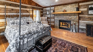 A log cabin bedroom with a four-poster bed, a stone fireplace, and a rustic wooden ceiling. - AUTHENTIC ANTIQUE LOG CABIN LOCATED IN TIMBERIDGE COMMUNITY (Gatlinburg)