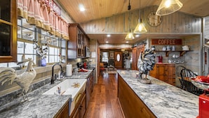 A kitchen with wooden cabinets, a marble countertop, and hanging lights. - AUTHENTIC ANTIQUE LOG CABIN LOCATED IN TIMBERIDGE COMMUNITY (Gatlinburg)