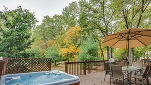 A hot tub on a wooden deck with a table and chairs, surrounded by trees.