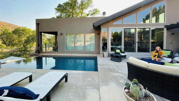 A modern outdoor pool area with lounge chairs, a seating area with cushions, and a large window overlooking a natural landscape. -  Beautiful Home with private Infinity Edge Pool 2 miles to ZNP main entrance (Springdale)