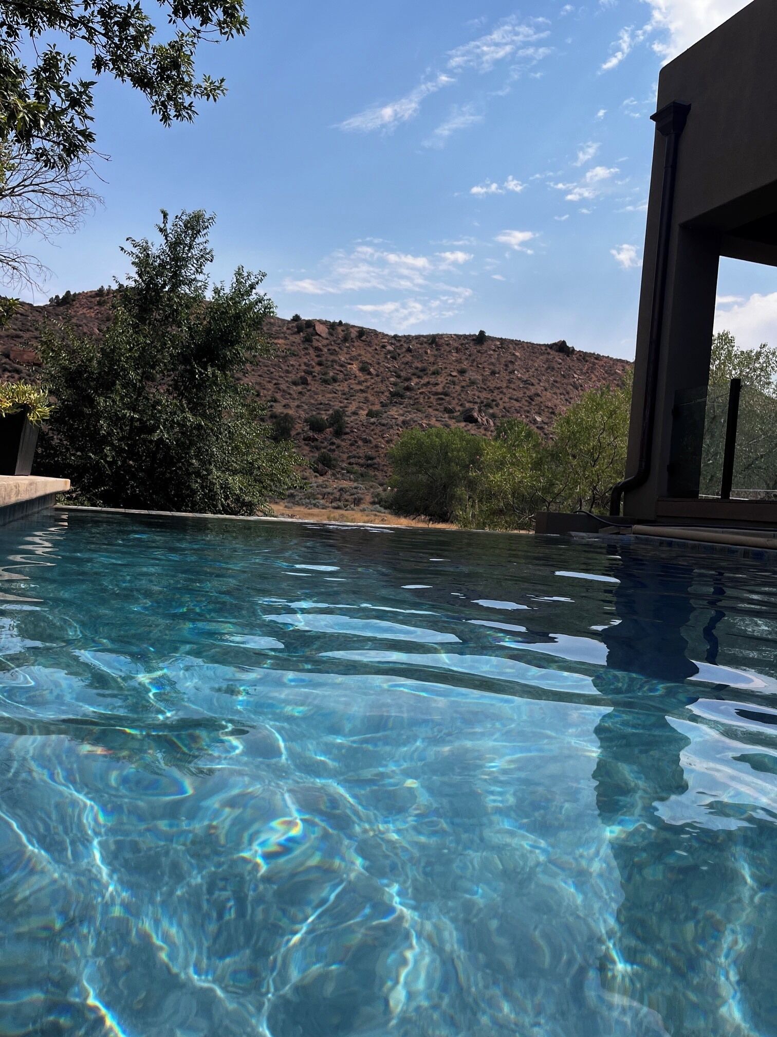 A clear swimming pool with a view of a hilly landscape and a building in the background.