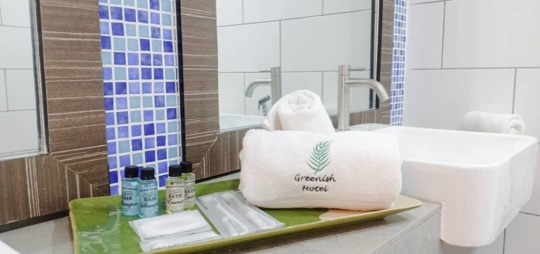 A bathroom with a white sink, a towel with 'Greenleaf Hotel' logo, and toiletries on a tray.
