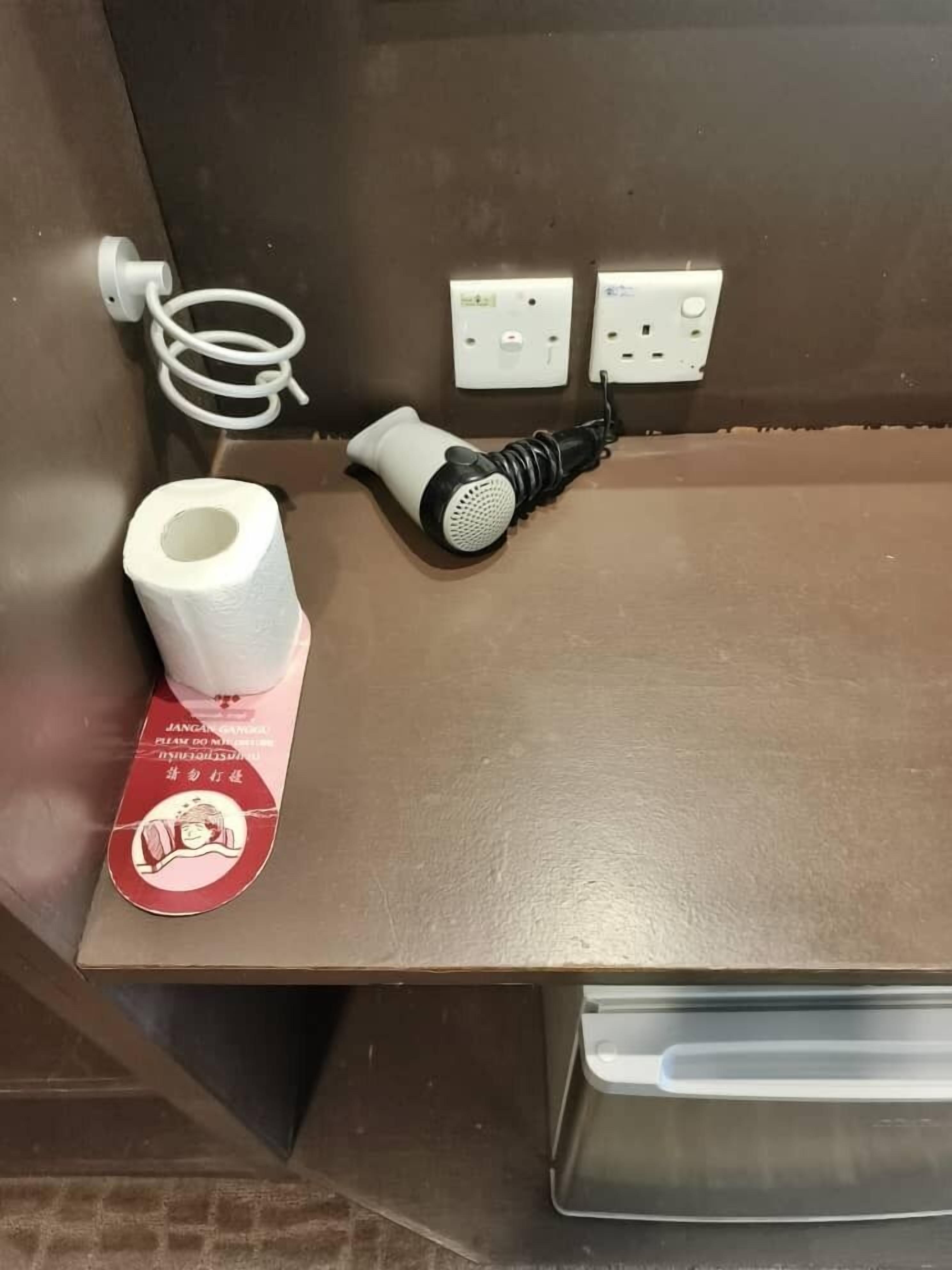 A bathroom with a towel dispenser, a paper towel dispenser, a hairdryer, and a trash bin.